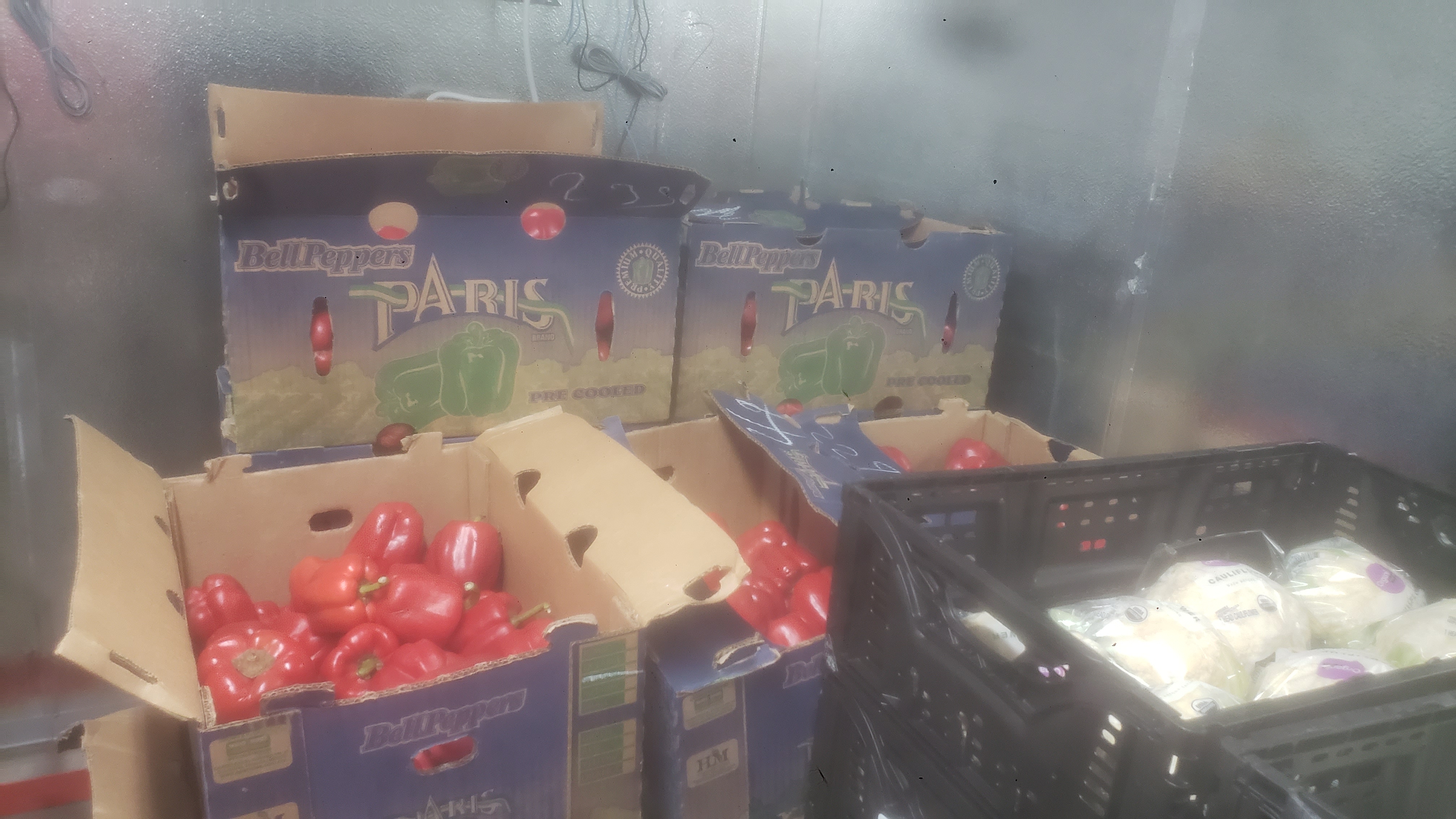 Cardboard boxes full of red bell peppers next to crates of packaged lettuce.